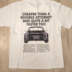 Vit t-shirt Porsche tryck S - Vit t-shirt med stort tryck på ryggen föreställande en Porsche och texten “Cheaper than a divorce attorney and quite a bit faster too”. Tillverkad i 100% mjuk bomull med klassisk passform och rund halsringning. 📏Storlek S längd: 65cm. Bredd: 46cm. Oanvänd i fint skick. Meddela vid frågor!