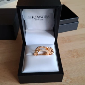 Guldiga örhängen från Sif Jakobs - Snygga guldpläterade örhängen från Sif Jakobs med glittrande stenar på framsidan och en cool, skulpterad design på baksidan. Perfekta hoops för dig som vill sticka ut med både elegans och edge. Kommer i original ask.