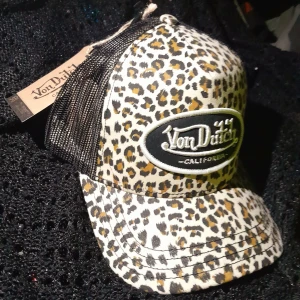 Von Dutch Keps  - Säljer en snygg keps från Von Dutch med leopardmönster och svart mesh på sidorna och baksidan. Kepsen har böjd skärm och broderad logga framtill. 
