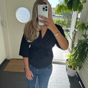 Svart omlottblus med knyt - Snygg svart omlottblus med knyt i midjan och trekvartsärmar! 