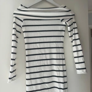 Randig offshoulder klänning Nelly - Säljer en vit och svart ribbad klänning från Nelly i storlek XS. Klänningen har offshoulder-design, långärmade ärmar och ett snyggt horisontellt randigt mönster. Materialet är mjukt och stretchigt. Använd endast en gång❣️