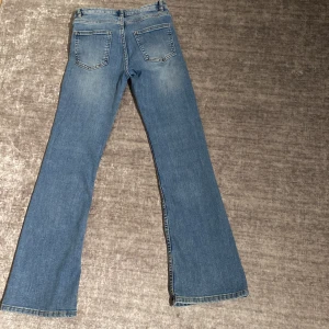 Blå bootcut jeans med ljus tvätt - Snygga blå jeans med bootcut-modell och ljus tvätt. Klassisk femficksdesign och normal passform. Perfekta för dig som gillar en retroinspirerad look med utsvängda ben. Jeansen har dragkedjegylf och är tillverkade i mjukt denimtyg.