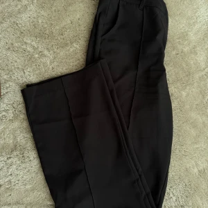 Svarta kostymbyxor med raka ben - Stilrena svarta kostymbyxor med raka ben och klassisk passform. Byxorna har hällor för bälte och fickor framtill. 