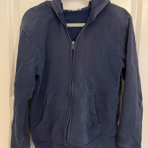 Mörkblå hoodie med dragkedja från H&M - Enkel och stilren mörkblå hoodie med dragkedja framtill och huva. Tröjan har två stora fickor på magen och långa ärmar. Perfekt för en avslappnad look och passar till det mesta. Materialet känns mjukt och bekvämt. storlek M /S för barn. 