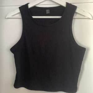 Svart ribbad linnetopp  - Säljer en svart ribbad linnetopp från Fresral i storlek S. Toppen är ärmlös med rund halsringning och croppad passform. Perfekt att matcha med jeans eller kjol för en clean och stilren look.
