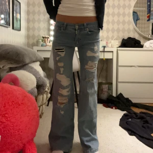 Ljusblå slitna jeans från Nelly, strl 34 - Ljusblå jeans från Nelly med rejält slitna detaljer och hål framtill. Modellen har låg midja och raka ben med loose fit. Klassisk femficksdesign och tillverkade i bomull. Perfekta för dig som gillar en avslappnad och trendig look. Helt nya och aldrig använda!