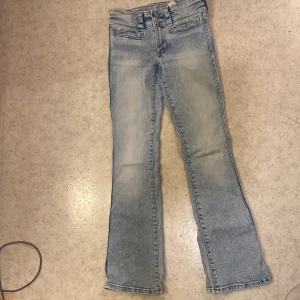 Bootcut ljusblå jeans med låg midja - Snygga ljusblå jeans med bootcut-ben och låg midja. Jeansen har justerbar midja, dubbla knappar och klassiska fickor fram. Perfekta för dig som gillar en avslappnad och trendig look. Storlek 152, passar ca 11-12 år.
