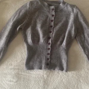 Grå ribbad kofta med knappar - Superfin grå kofta med ribbad midja och långa ärmar. Knappar hela vägen framtill i en matchande nyans. Perfekt till lager-på-lager och enkel att styla till olika outfits.