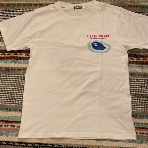 Vit BAPE t-shirt - Vit t-shirt från A Bathing Ape. Kvitto och original påse ingår. Max använd 10 gånger och har bara legat i några år, som nytt skick (slim fit) storlek M