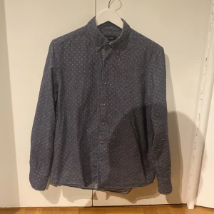 Blå prickig skjorta från Massimo Dutti - Snygg blå skjorta från Massimo Dutti med små vita prickar och klassisk krage. Jag säljer den då den inte passar min stil.                                                Skjortan har knappar framtill och är långärmad. Tillverkad i mjuk bomull som känns skön mot huden. Perfekt för dig som gillar stilrena detaljer och en modern look. Den kommer med extra knappar och ingen defekt förekommer. Tveka inte att fråga om du undrar något!!🙌🏽🙌🏽🙌🏽