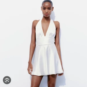Vit halterneck klänning från Zara - Supersnygg vit kort klänning från Zara i satinliknande material. Djup v-ringning, halterneck och knytning (rosett) i ryggen😍den är aldrig använd så den är verkligen som ny👌