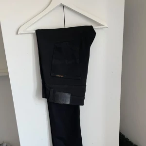 Svarta jeans från Nudie Jeans, 32/32 - Säljer ett par svarta jeans från Nudie Jeans i storlek 32/32. Modell lean dean. Klassisk femficksmodell med svarta sömmar och Nudie-logga på bakfickan. Jeansen har en stilren look och är tillverkade i bomull.  Pris kan diskuteras vid snabb affär.