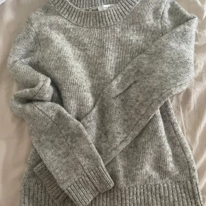 Grå stickad tröja från Zara - Mysig grå stickad tröja från Zara i storlek M. Tröjan har rund halsringning, ribbade muddar och är långärmad. Perfekt för lager-på-lager och chill dagar. Har lite smink vid halsen och därför säljs den billigare. Nypris 500kr