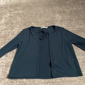 Mörkblå kofta med knyt från 157 - Mörkblå kofta från 157 med långa ärmar och söt knytning vid halsen. Enkel och stilren design som passar perfekt till lager-på-lager. Mjuk och skön i materialet, perfekt för kyligare dagar.