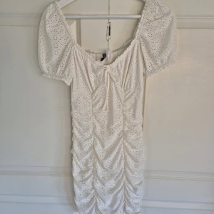 Vit klänning/off-shoulder klänning - Superfin vit kort klänning från H&M med puffärmar och v-ringning. Klänningen har broderade hålmönster, rynkade detaljer framtill och en söt knytning vid bysten. Går att bära som off-shoulder! Storlek S, endast använd vid ett tillfälle.