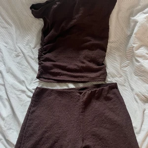 Brunt set - Säljer en brun oneshoulder topp med matchande byxor. Liknande det från Nelly. Helt oanvänt. 