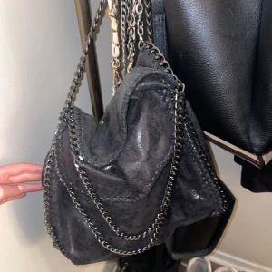 Svart axelväska med kedjedetaljer - Snygg svart axelväska med glansig finish och silvriga kedjor. Perfekt till skolan. Aldrig använd