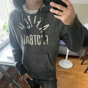 Mörkgrå hoodie Abercrombie & Fitch - Säljer en fet mörkgrå hoodie från Abercrombie & Fitch. Tröjan har några slitningar och färgen är riktigt snygg.