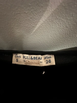 Svart/brun glittrig klänning  - Supersnygg svart/brun glittrig kortklänning från Pull&Bear med tunna axelband och v-ringad hals. Klänningen har ett heltäckande paljettmönster som ger en riktigt festlig look. Perfekt för dig som vill sticka ut och glänsa.