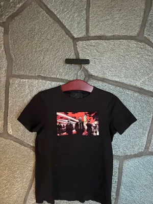 Svart Limitato t-shirt  - Svart t-shirt från Limitato med ett coolt grafiskt tryck på bröstet i rött, vitt och svart. Trycket visar en stadsmiljö med figurer och Big Ben i bakgrunden. T-shirten har rund hals och korta ärmar, tillverkad i mjuk bomull för skön passform.