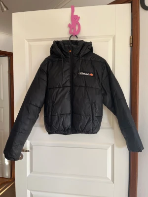 Svart pufferjacka från Ellesse - Svart varm pufferjacka från Ellesse, i storlek 32 med broderad logga på bröstet. Jackan är lätt croppad. Perfekt för vintern och kalla dagar! 