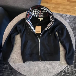 Svart Burberry hoodie - Helt ny burberry hoodie i storlek M. Fick den som present av farsan som var nere i frankrike. Den passade inte mig så därför säljer jag den. Den är värd mycket men säljer den för endast 999 kr för att kunna köpa en ny