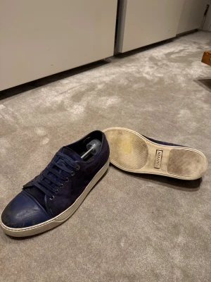Mörkblå sneakers från Lanvin - Snygga mörkblå sneakers från Lanvin med ovandel i mocka och tåparti i skinn. Storlek 8 (42). Skick 5/10 slitna på insidan och toecapen.