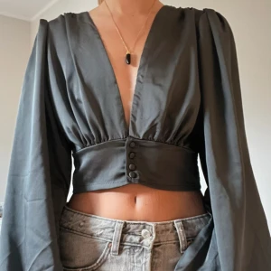 Grå croppad blus med knappar - Säljer en svart croppad blus med djup v-ringning och långa, vida ärmar