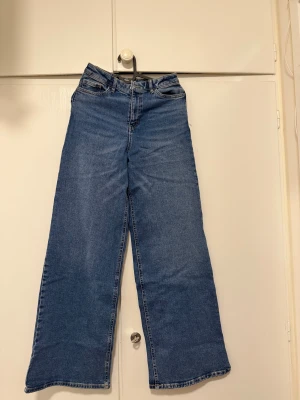Blå wide jeans från Lindex - Snygga blå jeans från Lindex i modell med breda ben och klassisk femficksdesign. Hög midja och dragkedja framtill. Perfekta för dig som gillar en avslappnad och trendig look. Tillverkade i mjukt denimtyg för skön känsla hela dagen.