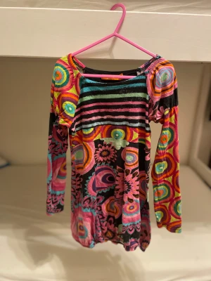 Färgglad mönstrad klänning Desigual - Supercool klänning från Desigual och massor av färgglada mönster i rosa, turkos, svart, gul och orange. Klänningen har både ränder och cirklar samt blommiga detaljer, perfekt för dig som gillar att sticka ut. Mjuk och skön bomullskänsla. Barn till tjejer 
