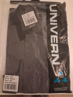 Grå arbetsjacka från Univern XXL - Säljer en grå arbetsjacka från Univern i storlek XXL. Jackan har flera praktiska fickor framtill, svart krage och axelparti. Materialet är en blandning av polyester och bomull, vilket gör den slitstark och bekväm. Perfekt för dig som vill ha en funktionell jacka med cool look.