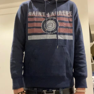 Saint Laurent Hoodie  - Säljer nu en marinblå Saint Laurent hoodie som är sjuuuukt eftertraktad. Den säljs inte i butik längre vilket gör den mer rare. Osäker på äkta men annars är Nypris|| 8000 || Mitt pris|| 1299 || Kan gå ner i pris! Nästan helt ny, använd 1-2 gånger. Storlek S och modellen är 176 och väger 56! Skriv gärna frågor! 
