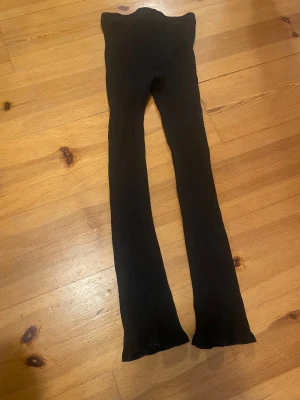 Svarta ribbade leggings från H&M - Svarta ribbade leggings från H&M med stretchig passform och smal siluett. Materialet är mjukt och följsamt, perfekt för en chill och stilren look. Midjan är elastisk och benen är långa med lätt utsvängda avslut. Snygga att matcha med oversized hoodie eller crop top.