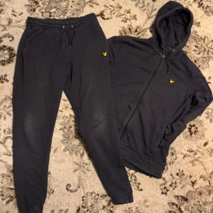 Svarta mjukisbyxor från Lyle & Scott - Säljer ett par svarta mjukisbyxor från Lyle & Scott med gul fågel-logga på höften. Byxorna har snörning i midjan, elastiska muddar vid bensluten och är gjorda i mjukt bomullsmaterial. Perfekta för chill eller träning.