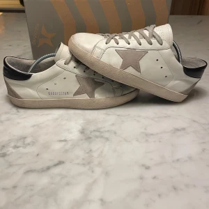 Golden Goose vita sneakers med stjärna - Golden Goose sneakers i vitt skinn med grå mockadetaljer och en ikonisk stjärna på sidan. Har används några gånger och skada är creasing. skon kostar 5800 nypris. Perfekt som vill ha en snygg stilren look till vardagen.                                  Skriv vid frågor, priset är inte hugget i sten🤝