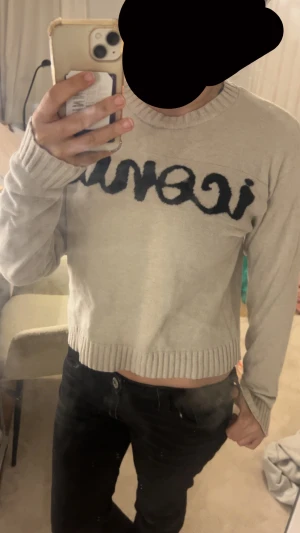 Beige stickad tröja med svart text - Säljer en beige stickad tröja från Iconic med svart broderad text över bröstet. Tröjan har rund hals, ribbade muddar och lång ärm. Passformen är loose och den är lite croppad i modellen. Perfekt för dig som gillar statement-plagg