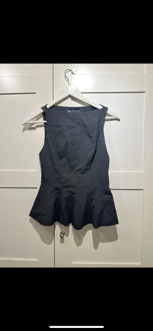 Svart peplum topp från Zara - Snygg svart ärmlös topp från Zara med peplumskärning som ger en cool siluett. Toppen har rund hals och är tillverkad i ett mjukt bomullsmaterial. Har tyvärr ingen bild hur den sitter på eftersom den är för liten för mig.
