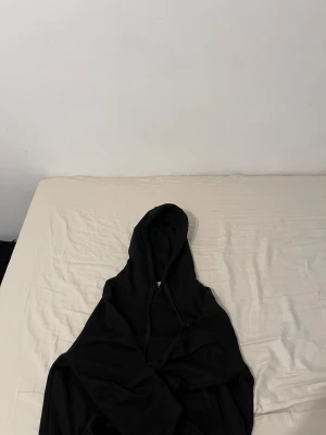 Svart hoodie från Stone Island - Svart hoodie från Stone Island med klassisk logotyp-patch på ärmen. Tröjan har huva med snörning och är tillverkad i mjuk bomull. Perfekt för dig som gillar streetwear och vill ha en clean look med exklusiv känsla.