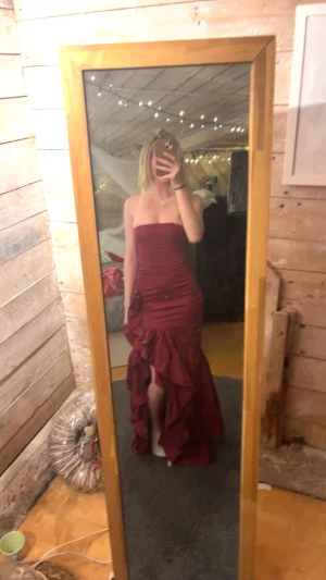 Vinröd långklänning från Babyboo XS - Säljer en vinröd långklänning från Babyboo i storlek XS. Klänningen är axelbandslös med figurnära passform, har en snygg slits framtill och volangdetaljer längs kjolen. Materialet är skönt och stretchigt, perfekt för att sticka ut på bal eller fest.