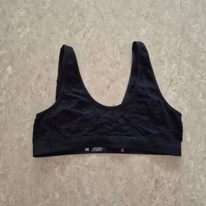 Sport-bh - Svart sport-bh från Cubus i storlek M. Sport-behån har breda axelband och ärmlös design, med snygga spetsdetaljer över hela framsidan och baksidan. Materialet är en mix av polyamid, polyester och elastan som ger en mjuk och stretchig känsla.