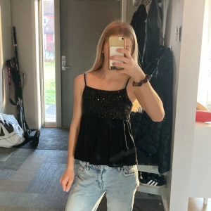 Svart glittrig linne-topp med paljetter - Säljer en jätte snygg svart linne-topp med smala axelband och glittriga paljetter över bysten.🤩 Toppen har en flowy passform nedtill och är perfekt för dig som vill sticka ut. ⭐️Materialet känns mjukt och toppen är lätt att matcha med både jeans och kjol.  Säljer den eftersom den har blivit för liten och används fåtalgånger☺️ skriv om det är några frågor! Priser kan diskuteras