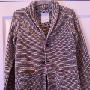 Grå baige stickad kofta från Zara - Säljer en grå baige stickad kofta från Zara med snyggt mönstrad insida. Koftan har två framfickor, knappar framtill och en mjuk, krage som ger en chill vibe. Perfekt för dig som gillar enkel men stilren design. 