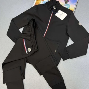 Svarta mjukisbyxor från Moncler - Svarta mjukisbyxor från Moncler med elastisk midja och ribbade benslut. Snygga detaljer med röd, vit och blå rand vid dragkedjan och Moncler-logga på benet. Perfekta för en chill och sportig look.