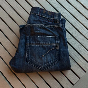 Blå jeans från Dondup med raka ben - Snygga blå jeans från Dondup med klassisk femficksdesign och raka ben. Jeansen har kontrastsömmar, slitningar vid fickorna och metallknappar. Materialet är robust denim och passformen är normal. Perfekt för dig som gillar en stilren och tidlös look.