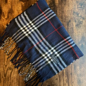 Burberry halsduk - Klassisk Burberrys-halsduk i 100% lammull, tillverkad i England. Mjukt och varmt material i ikoniskt rutmönster. Passar både dam och herr. I mycket bra skick små fläckar eller utan hål – perfekt för höst och vinter. 