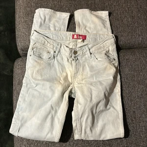 Ljusblå jeans - Säljer ett par ljusblå jeans från &Søn med klassisk femficksdesign och knappstängning. Jeansen har raka ben och normal passform, tillverkade i mjukt bomullsmaterial. Perfekt för dig som gillar en clean och enkel stil.