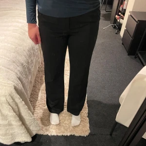 Svarta kostymbyxor med raka ben - Snygga svarta kostymbyxor med raka ben och klassisk passform. Byxorna har diskreta fickor bak och en stilren midja utan synliga detaljer. Perfekta för en clean och stilren look, passar till både skjorta och t-shirt.