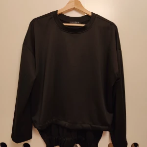 Svart loose sweatshirt med resår - En svart oversized sweatshirt från D'style Box med rund halsringning och långa ärmar. Tröjan har en cool resårdetalj nedtill som ger en snygg och avslappnad passform. Perfekt för en chill och trendig look.