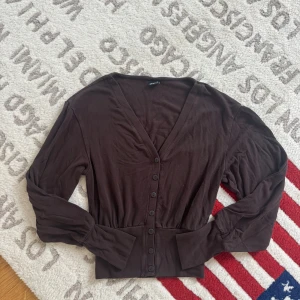 Brun kofta från Gina Tricot XS - Mysig brun kofta från Gina Tricot i storlek XS. Koftan har v-ringad hals, långa ärmar och knappar hela vägen framtill. Perfekt att slänga över en topp för en chill look. Materialet känns mjukt och lätt, och den har en snygg, lite loose passform.