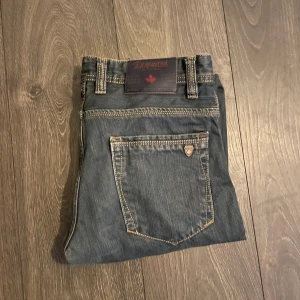 Dsquared2 blå jeans W30 - Snygga blå jeans från Dsquared2 i klassisk femficksmodell med kontrastsömmar och metallmärke på bakfickan. Jeansen har rak passform och normal midja, tillverkade i slitstarkt denim. Perfekta för dig som gillar stilrena och coola jeans.